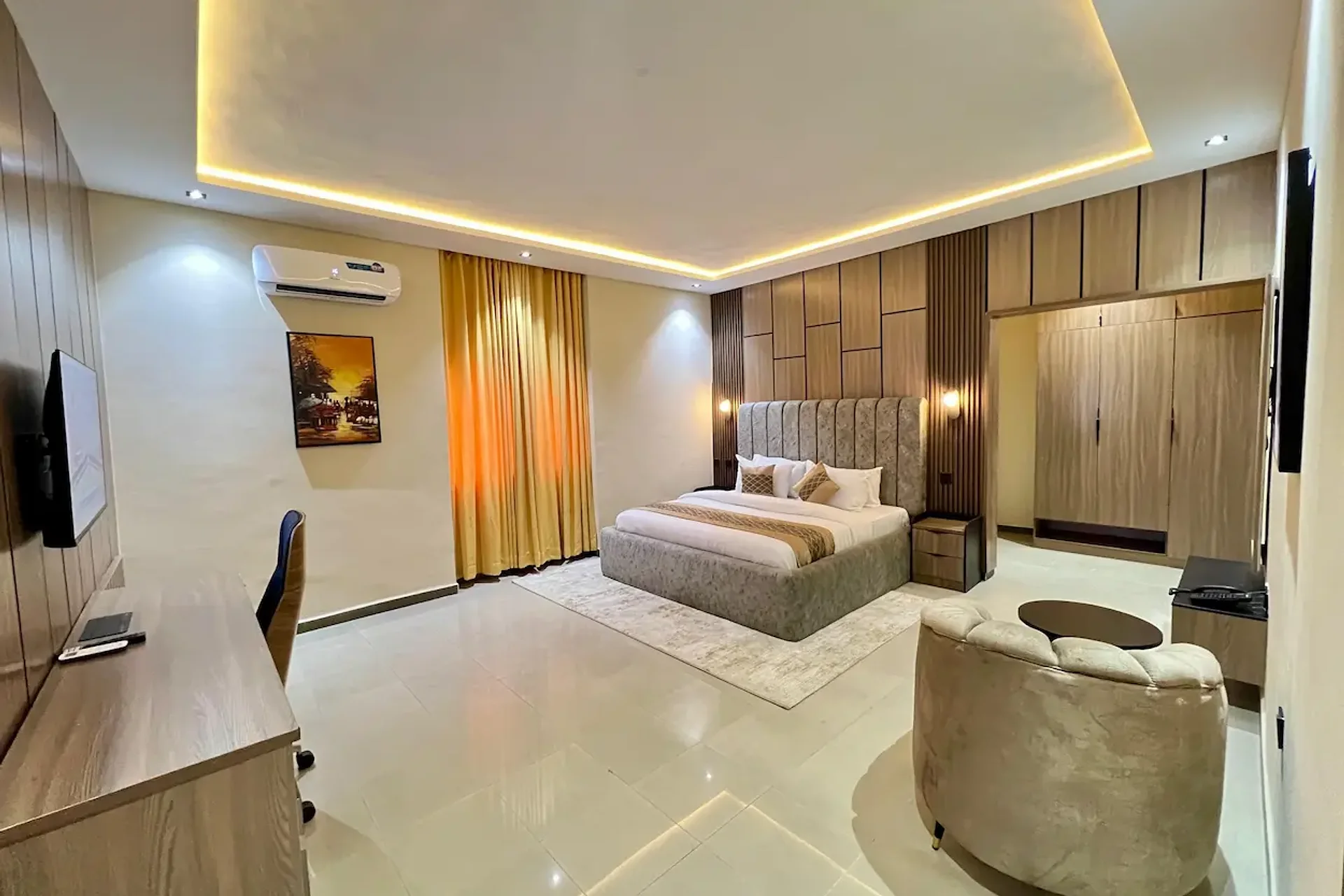 Rivona Hotels bedroom with gold curtains, grey headboard, and warm ceiling lighting